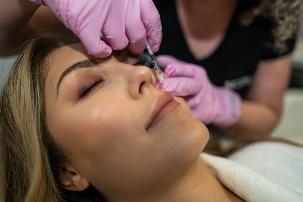 A practitioner placing dermal filler beside a patient’s nose